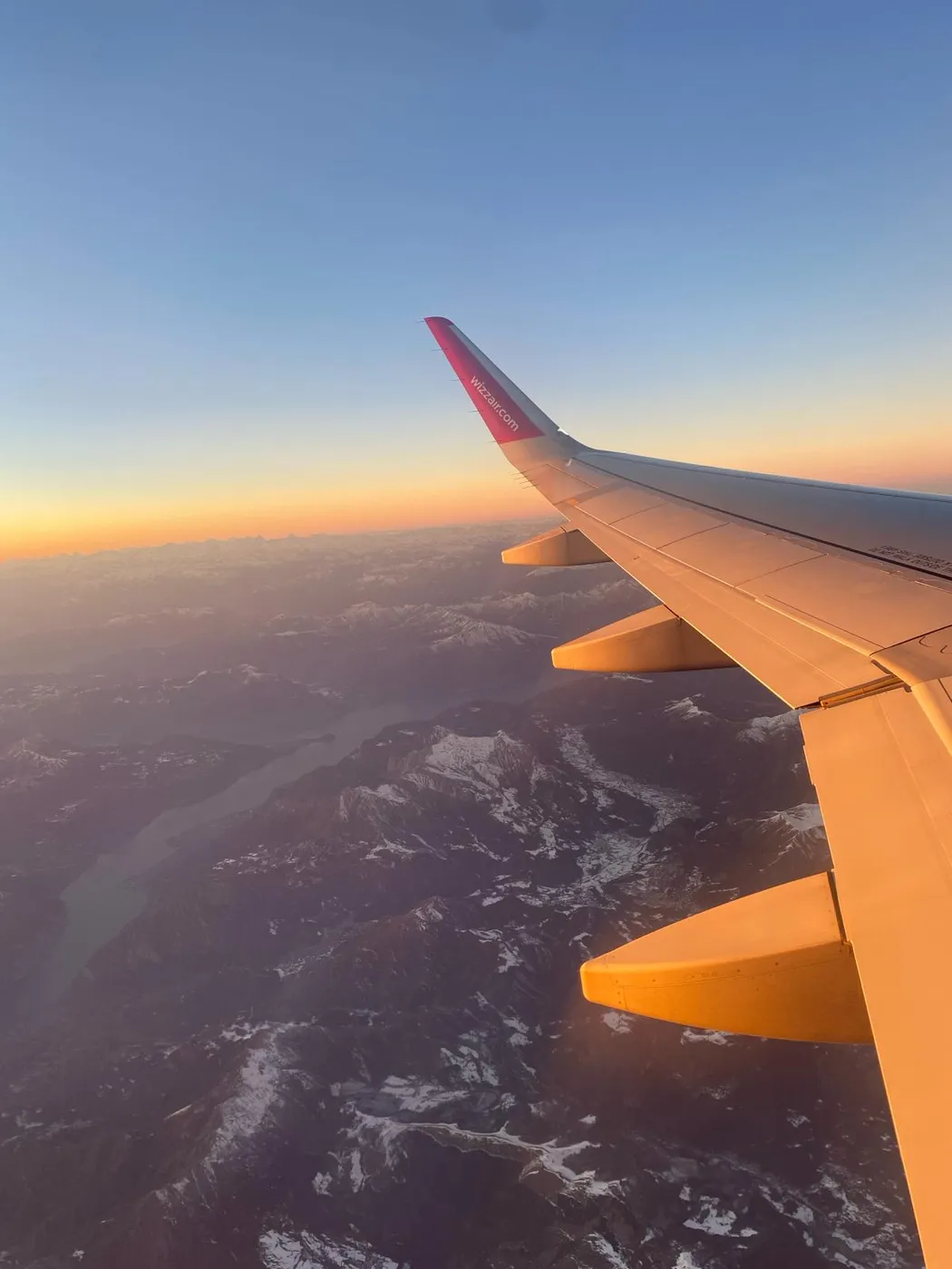 Blick aus dem Flugzeug über die schneebedeckten Alpen und einen oberitalienischen See im Abendlicht