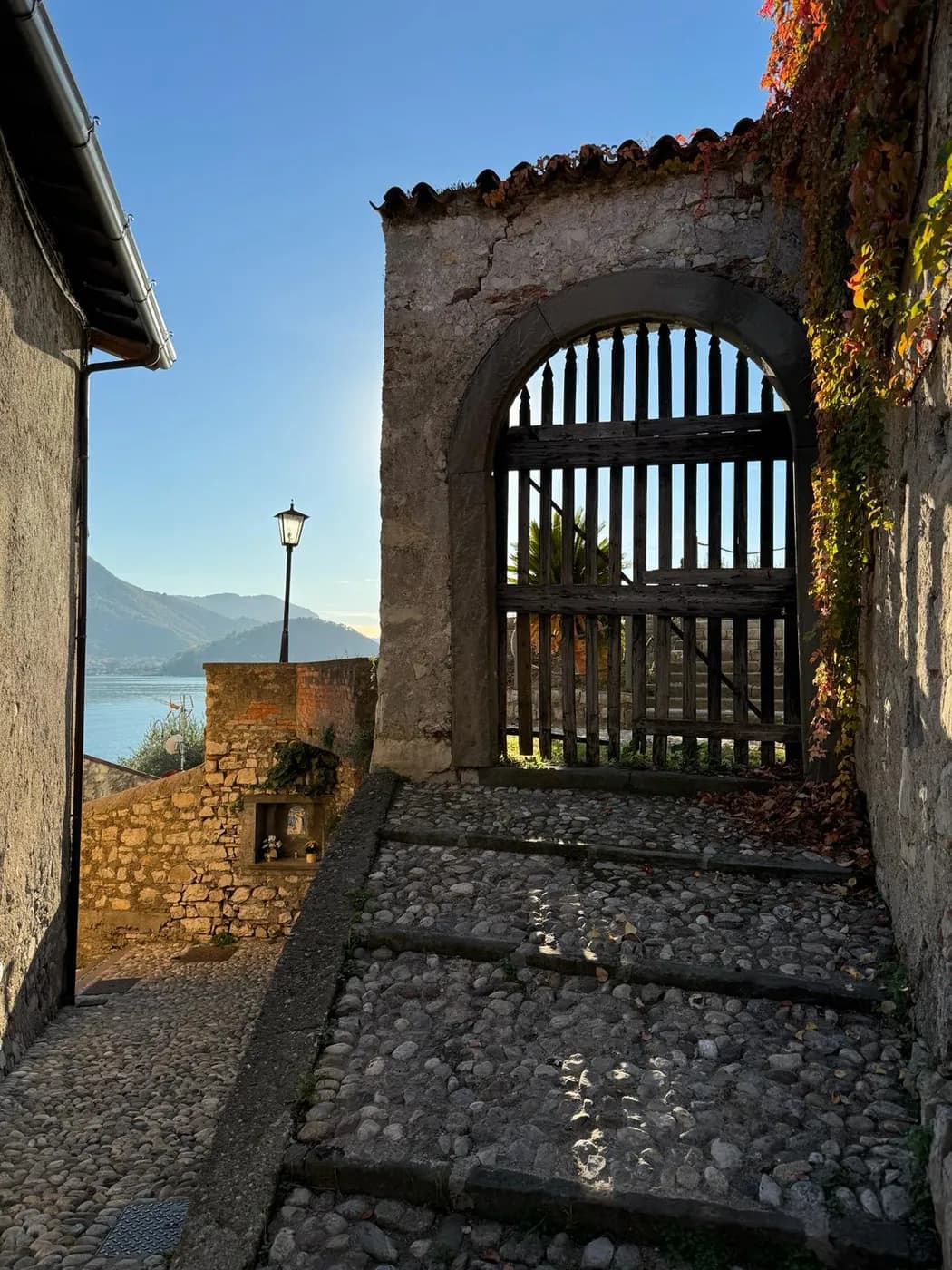 Gepflasterte Gasse mit steinernem Torbogen und Seeblick auf Monte Isola