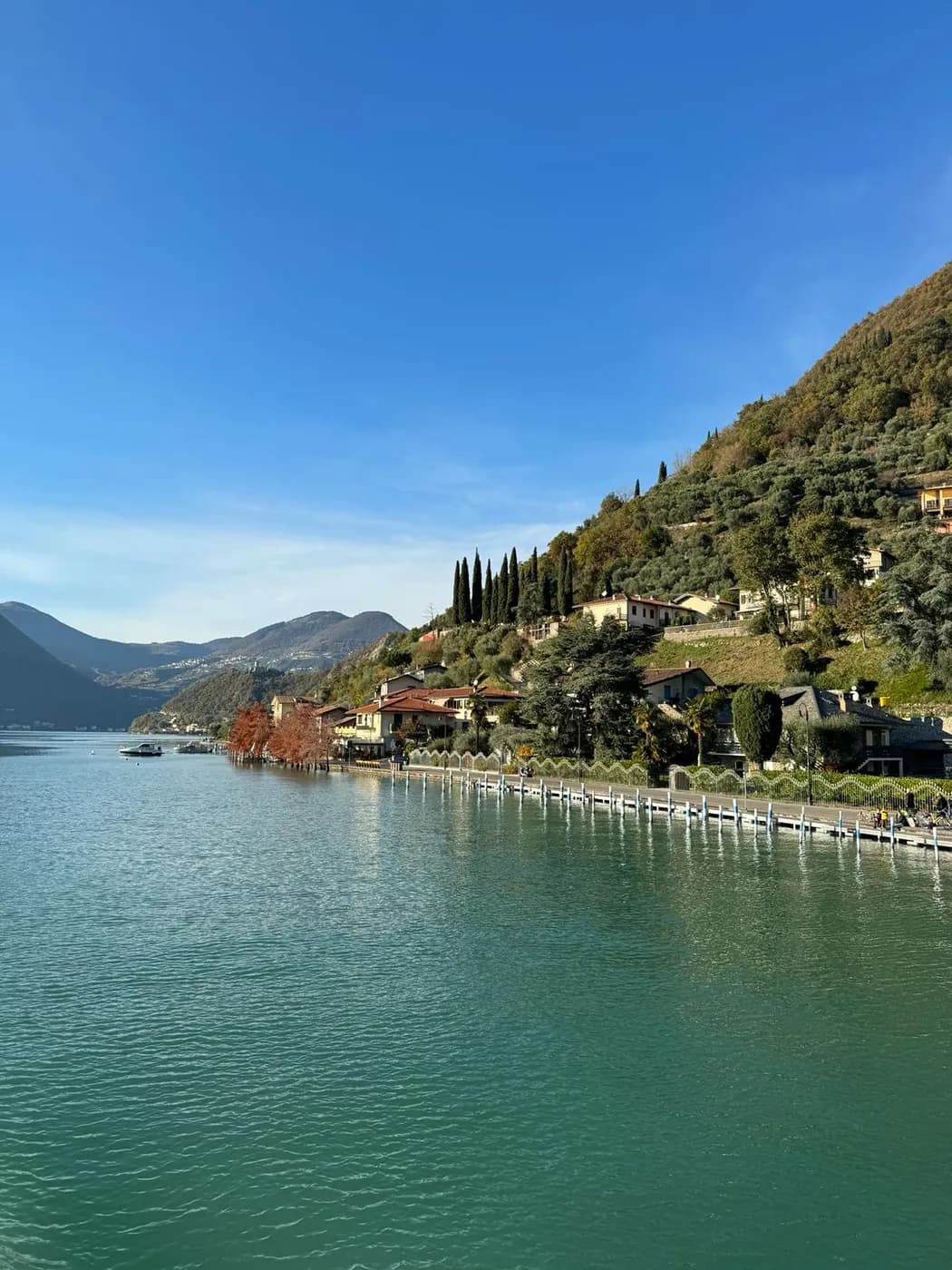 Uferpromenade eines Dorfes auf Monte Isola mit Zypressen und Bootssteg