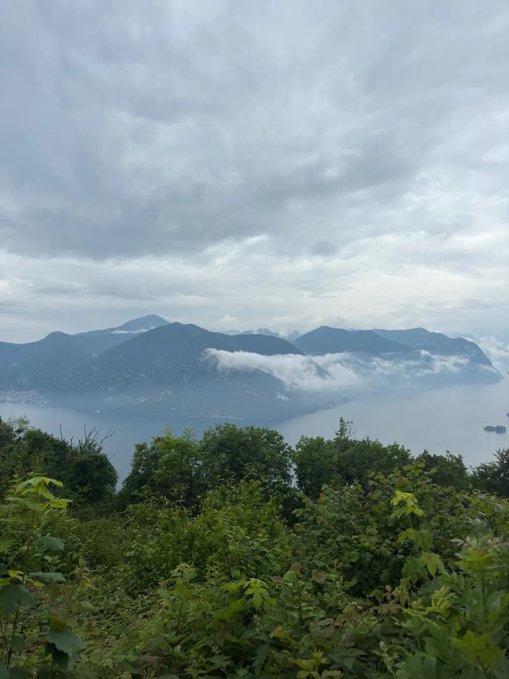 Aussicht von einer Anhöhe über den Lago d'Iseo mit Wolken und grünem Vordergrund